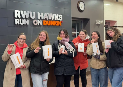 A picture of the author with 5 other girls. They are holding donuts and in front of a sign that says "RWU hawks run on dunkin"